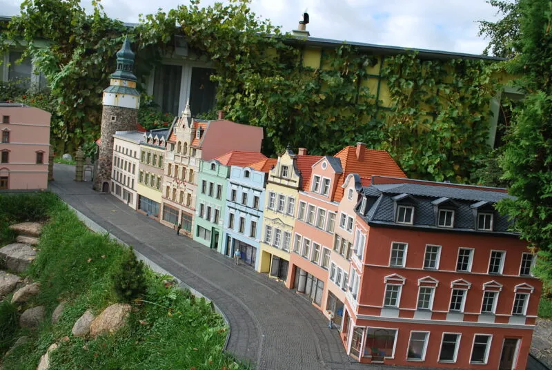 Miniatury kolorowych kamienic. Ich rząd kończy kamienna okrągła wieża.