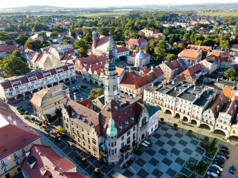 Zdjęcie z drona przedstawiające prostokątną płytę rynku z neorenesansowym budynkiem ratusza oraz okalające ją arkadowe kamieniczki i śródmiejską zabytkową zabudowę.