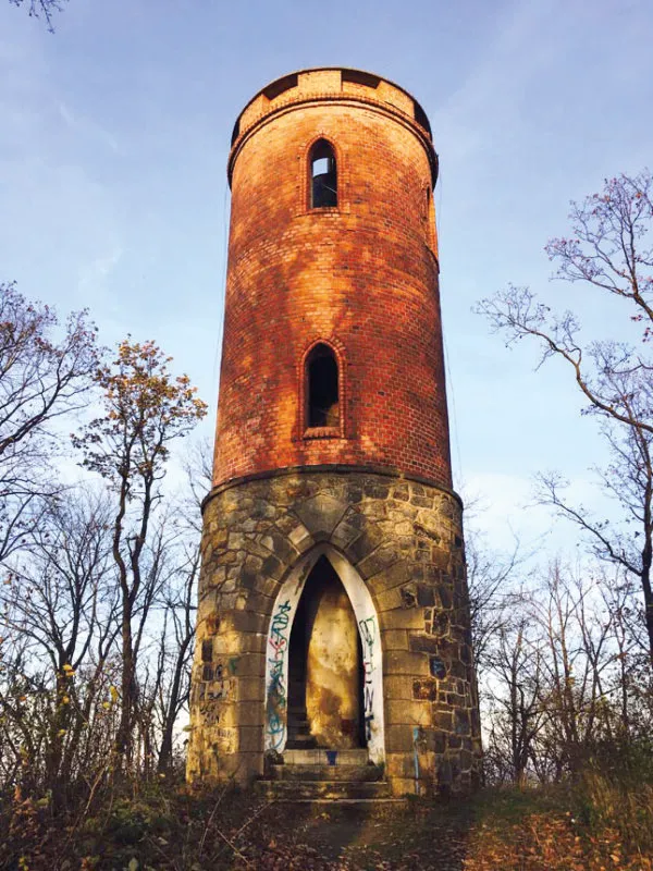 Jesienny widok z poziomu gruntu na zabytkową kamienno-ceglaną wieżę widokową na tle nieba