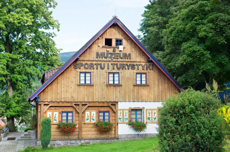 Drewniany dom z granatowymi zdobieniami okiennic i dachu. Na nam napis" Muzeum Sportu i Tyrystyki.