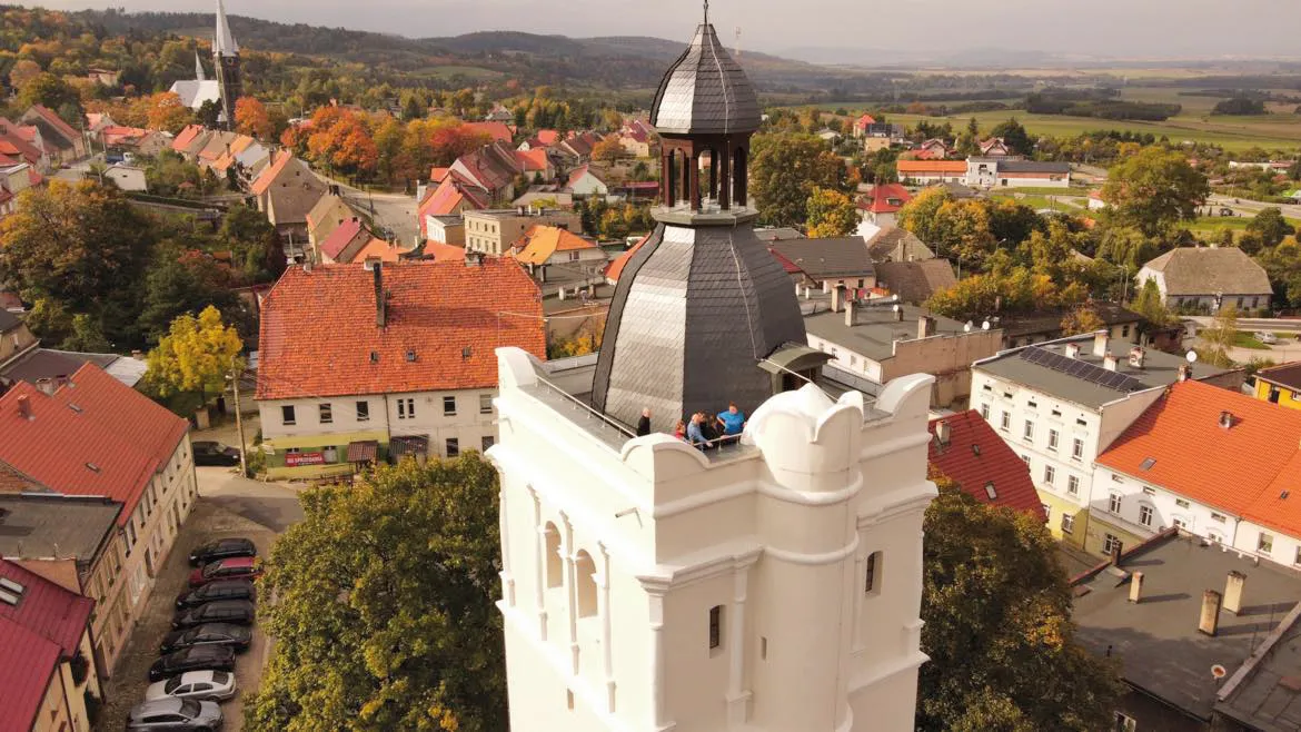 Widok z poziomu szczytu białej wieży widokowej w Złotym Stoku z okolic złotostockiego rynku. Widoczna panorama Sudetów i okolic Złotego Stoku.