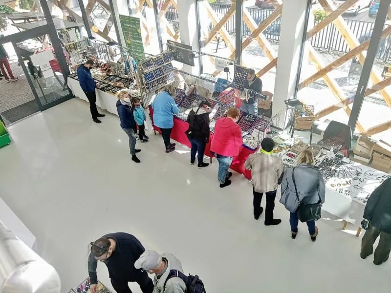 Wnętrze Centrum Obsługi Ruchu Turystycznego "Akwarium"w którym znajdują się ludzie stojący przy różnych stanowiskach informacyjnych. Na zdjęciu widać przeszklone szyby a w środku jest jasno
