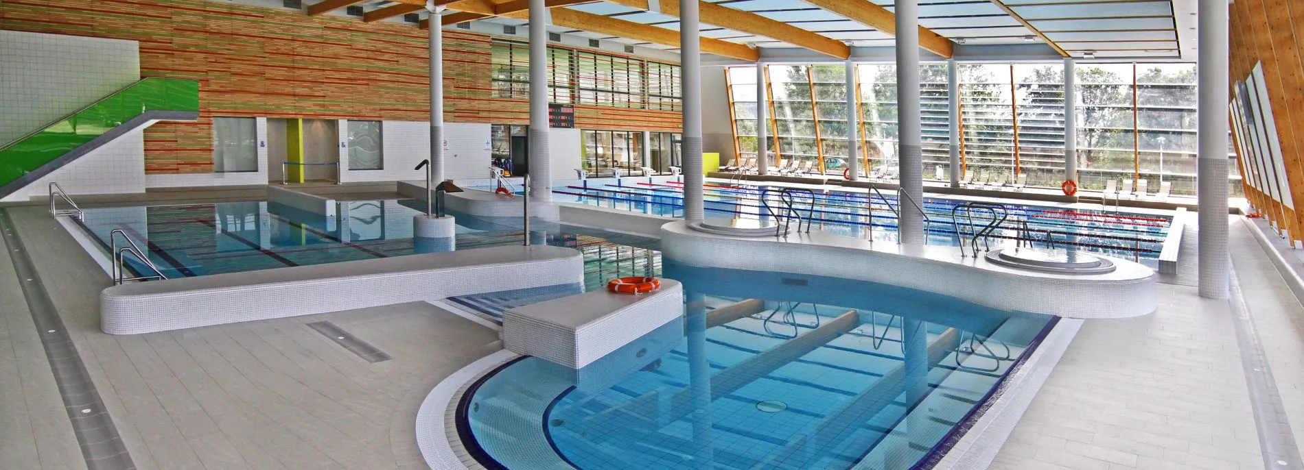 Trzy niecki basenowe w części sportowo-rekreacyjnej hotelu. Przeszklone ściany i elementy drewniane.