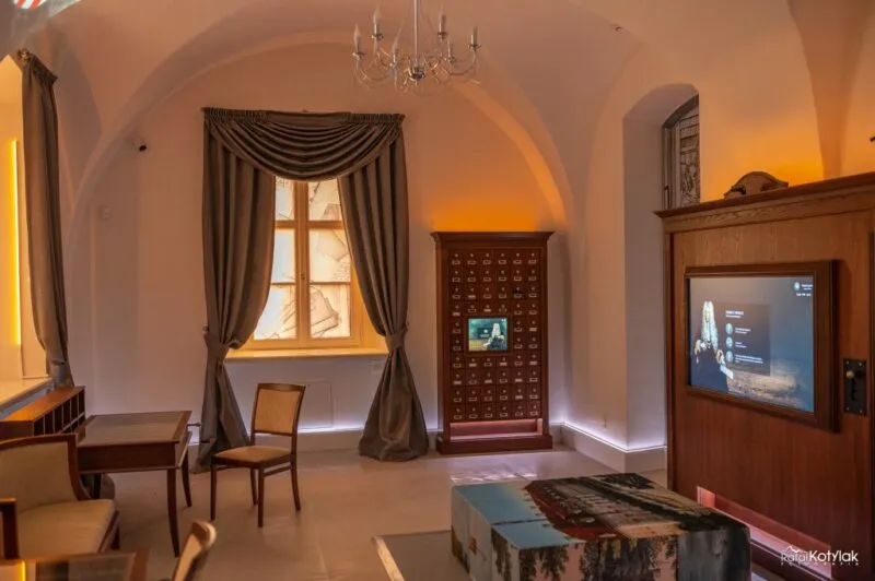 La salle intime du Centre naturel et éducatif de Sobieszów possède un intérieur voûté, un écran tactile, des meubles en bois et une exposition sous une lumière chaude.