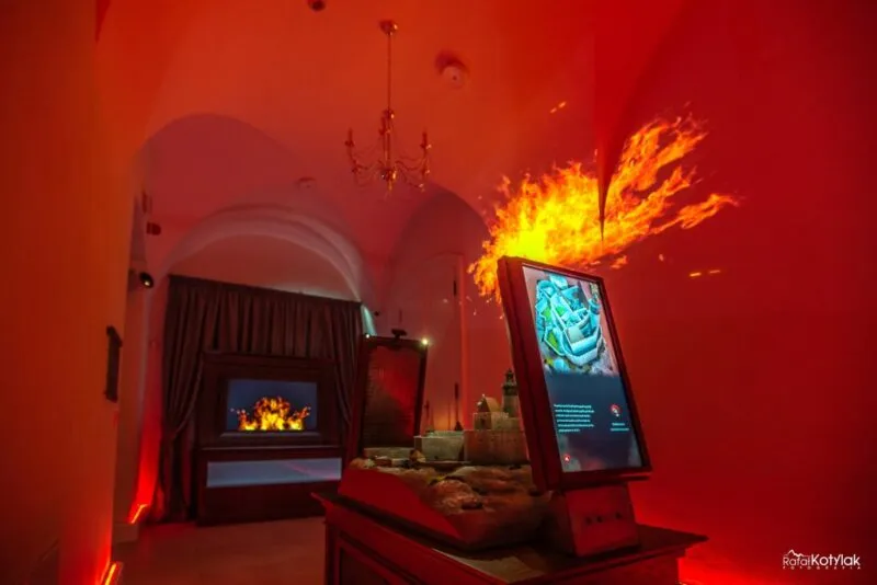 Une projection rouge de flammes remplit le mur de la salle assombrie du Centre naturel et éducatif de Sobieszów, à côté de l'écran interactif et de la vitrine.