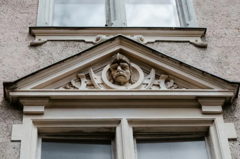 Detal ozdobny kamienicy prezentujący głowę nad oknem przy elewacji kamienicy
