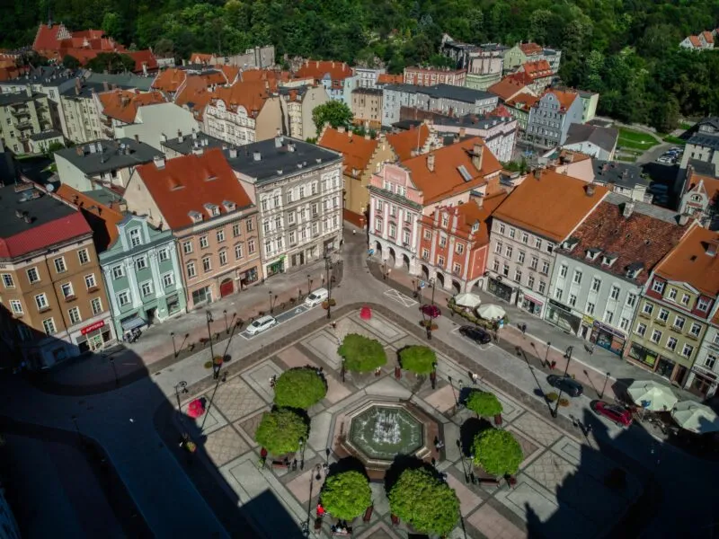Zdjęcie z Drona przedstawiające stare zabytkowe kamienice, których pośrodku znajduje się zadbany plac z liczną zielenią, drzewami