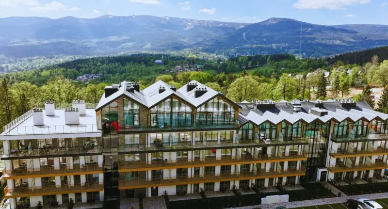 Widok z lotu ptaka na resort - elegancki budynek o przytulnym górskim charakterze, z dużymi oknami i balkonami, w tle góry.
