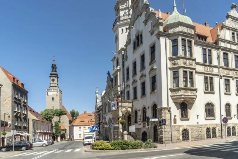 Widok na budynki, ratusz i ulicę w mieście, w tle niebieskie niebo.