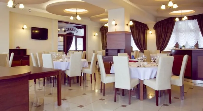 Sala restauracyjna ze stolikami nakrytymi estetycznymi, białymi obrusami oraz przylegające doń krzesła w białych pokrowcach.