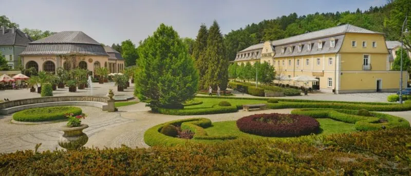 Budynek uzdrowiska z elegancką, historyczną fasadą, ozdobioną detalami w duchu architektury uzdrowiskowej, otoczony pięknym parkiem.
