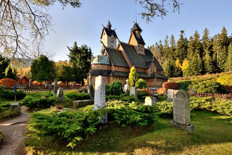 A photo of a small wooden church surrounded by a historic cemetery and nature