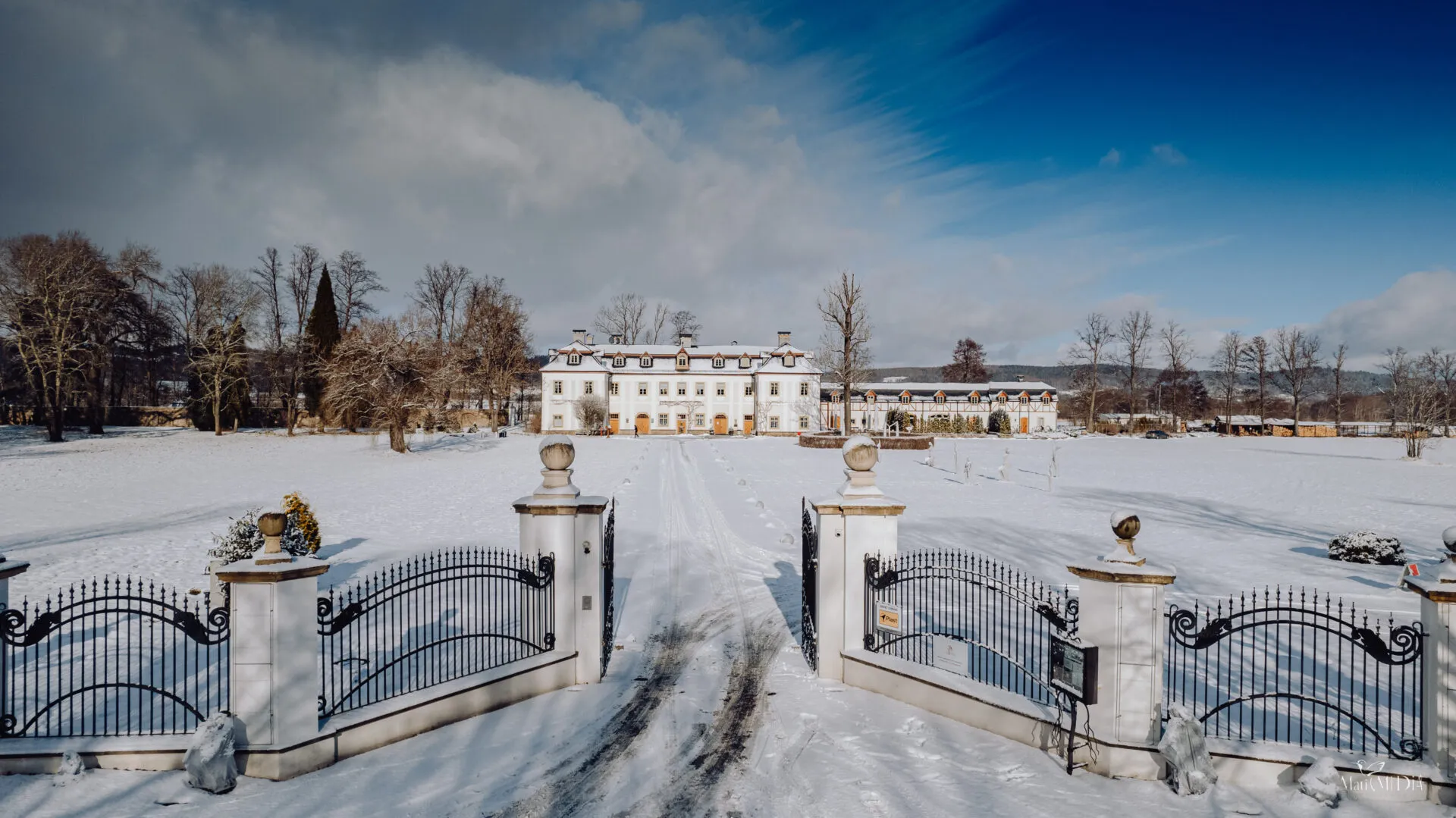 Widok na pałac w oddali, przed nim ogrodzenie. Cały trawnik pokryty śniegiem.