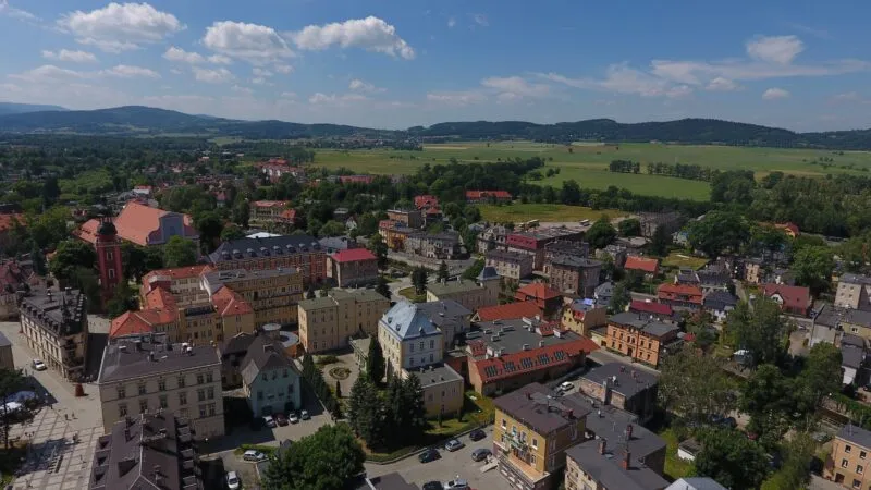 Widok na miasto z lotu ptaka, w tle góry, błękitne niebo.