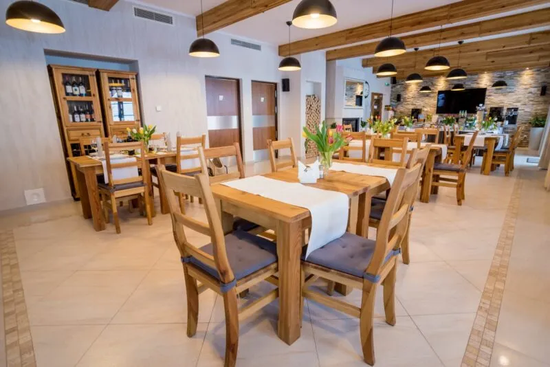Wnętrze sali restauracyjnej, z drewnianymi stolikami i drewnianymi krzesłami. 