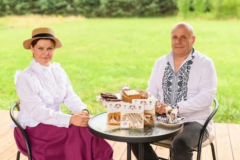 Kobieta i mężczyzna w śląskich strojach ludowych siedzą przy stoliku z piernikami