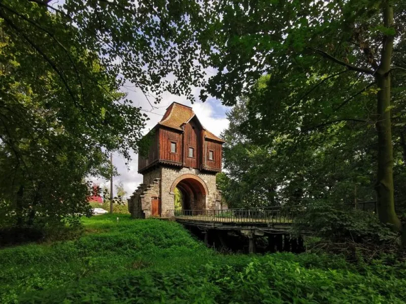 Kamienna brama przy moście z drewnianym domkiem na sobie.