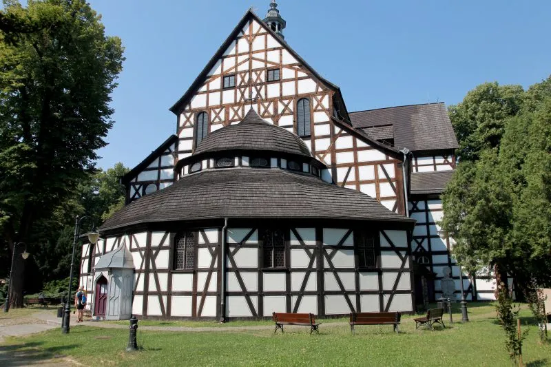 La Chiesa della Pace di Świdnica presenta una caratteristica struttura a graticcio bianca e marrone, un portico poligonale e un tetto ripido tra alberi alti.