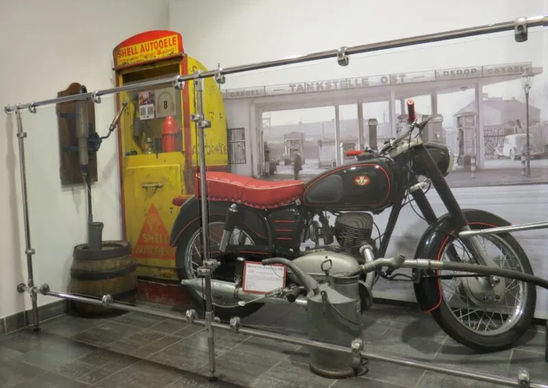 Stary motor w kolorze czarno czerwonym ustawiony na ekspozycji za szybą na tle białej ściany