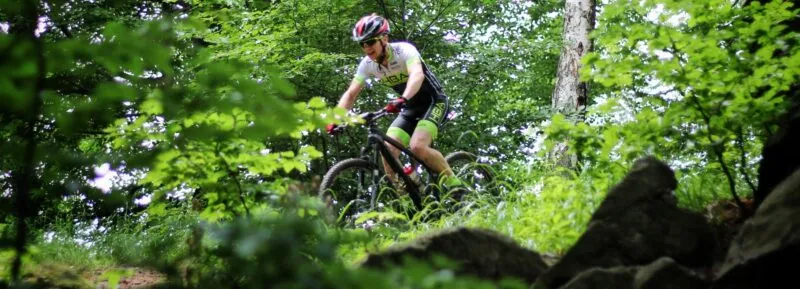 Rowerzysta w kasku na rowerze MTB jadący w nierównym terenie w lesie