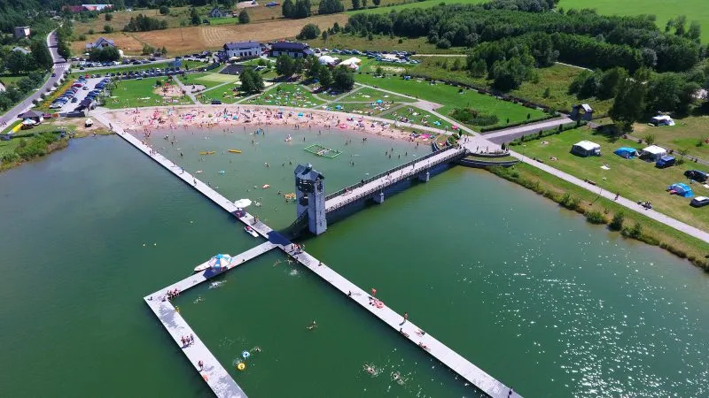 La vista a volo d'uccello mostra il bacino idrico di Stara Morawa con la zona balneabile, i pontili galleggianti e la torre, circondato dalla spiaggia, prati, parcheggi e campi.