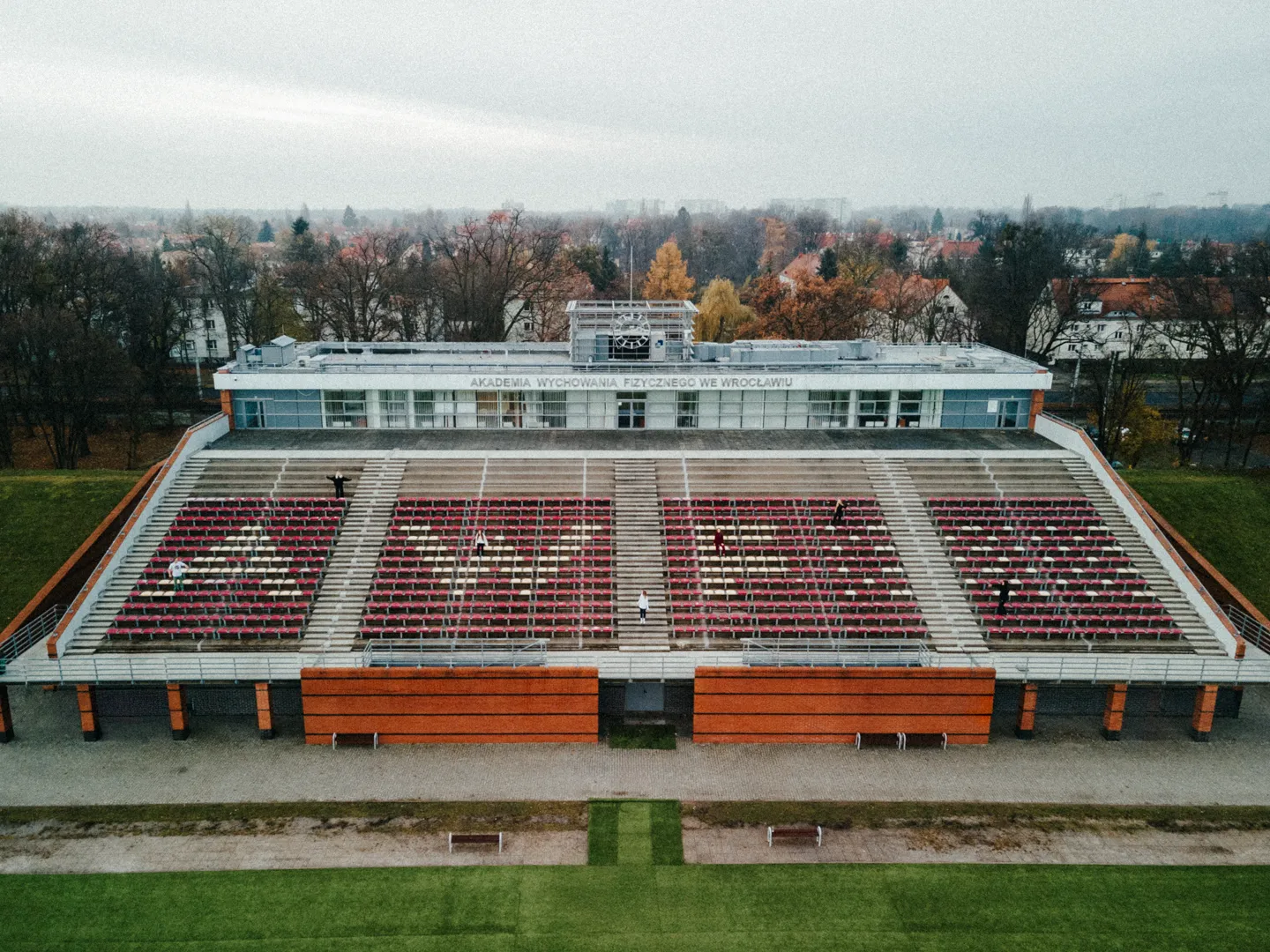 Widok na truby przy stadionie na terenie akademii wychowania fizycznego, krzesła trybun są czerwone a niektóre z nich białe, tworzą napis AWF