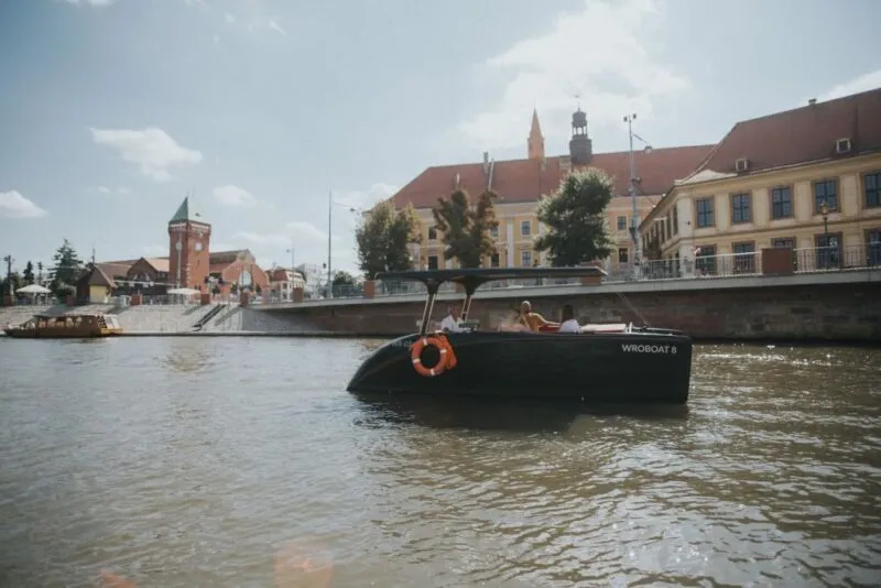 Widok na rzekę Odrę i płynącą po niej łódź a w tle budynek Hali Targowej