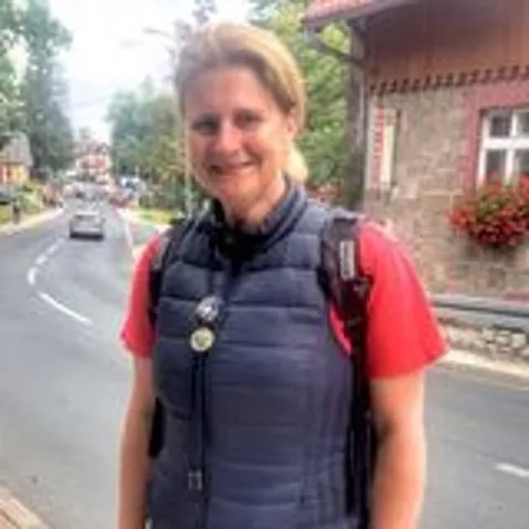 kobieta w czerwonym tshircie i szarej kamizelce stojaca przy szerokiej drodze