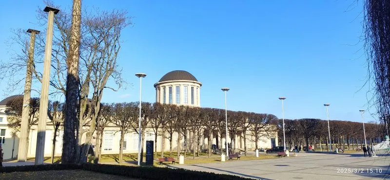Modernistyczny budynek o prostych, geometrycznych kształtach, wyróżniający się czterema charakterystycznymi kopułami na dachu, otoczony przestronnym terenem.