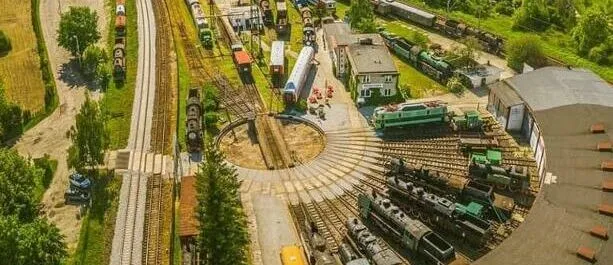 Zdjęcie z drona przedstawiające rozległą bocznicę kolejową wraz z terenem byłej parowozowni oraz towarzyszącej infrastruktury technicznej.