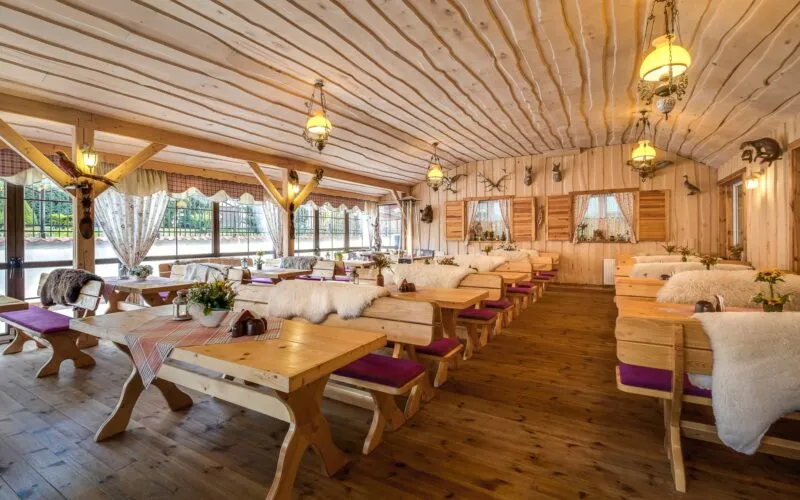 Sala restauracyjna w stylu góralskim, wykonana cała w drewnie, ze stołami i podłużnymi drewnianymi ławami.