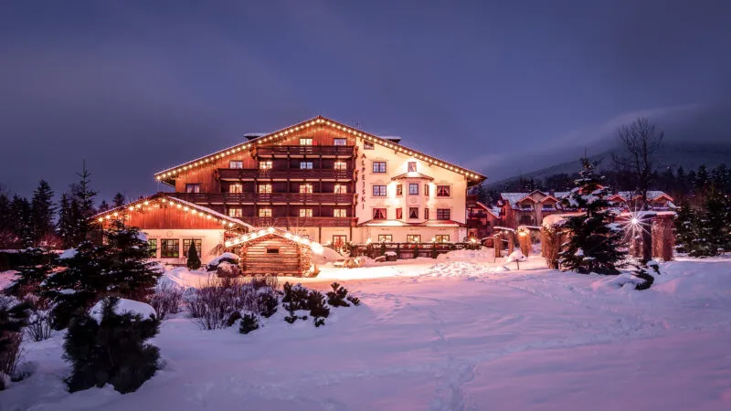 Budynek hotelu w stylu tyrolskim na tle nocnego nieba. Sceneria zimowa.