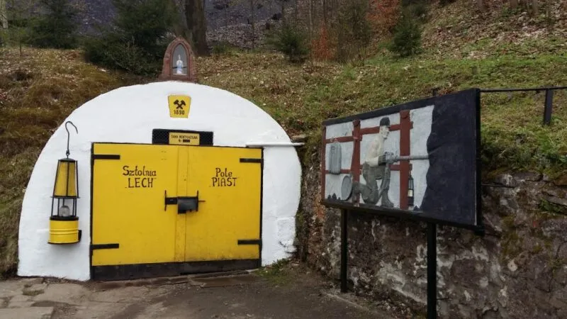Wejście do kopalni z żółtymi wielkimi drzwiami w otoczeniu zieleni.