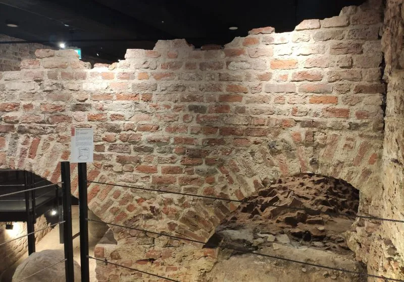 Fragment starego muru z cegły z łukiem, prawdopodobnie część fortyfikacji. Jest dobrze oświetlony i zabezpieczony barierkami.