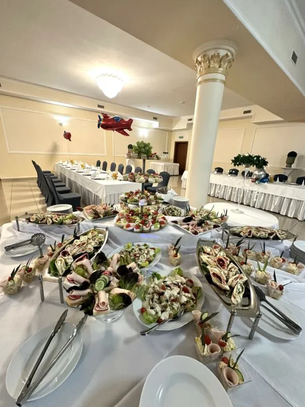 Wnętrze sali restauracyjnej (balowej), z widokiem na stół zastawiony zimnymi przekąskami.