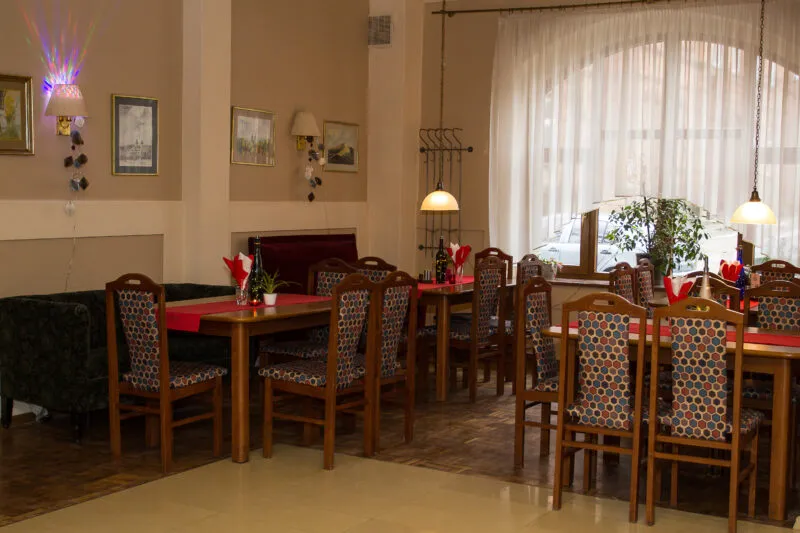 Sala jadalna z kilkoma stołami, przy których, przy każdym stoi od 4 do 6 krzeseł