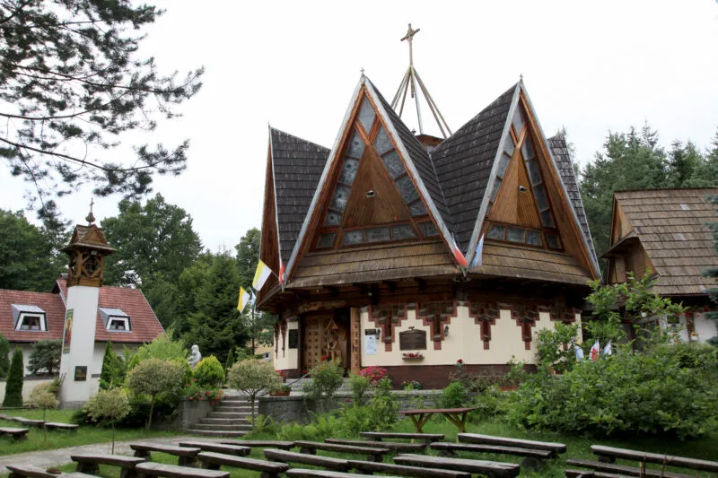 Niewielka, neogotycka budowla z cegły, z charakterystycznym, ostrym dachem i detalami architektonicznymi, otoczona zielenią