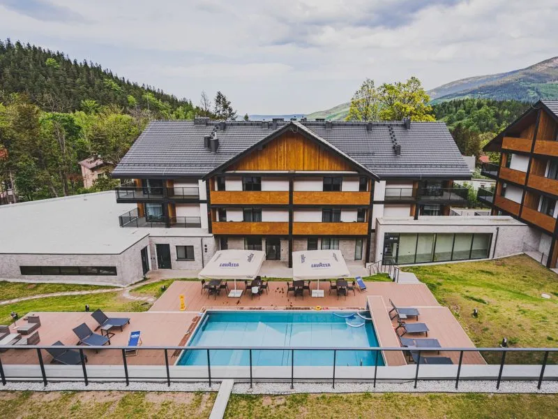 Widok na budynek hotelu z widocznym basem i z górami w tle