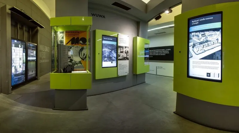 Wnętrze Visitor Centre przy Hali Stulecia wypełniają zielone stanowiska multimedialne, podświetlane mapy i ekrany z informacjami o kompleksie.