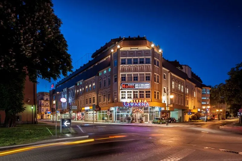 Zdjęcie dużego budynku narożnego, wykonane wieczorem. Budynek podświetlony, 4-kondygnacyjny, zrewitalizowany.