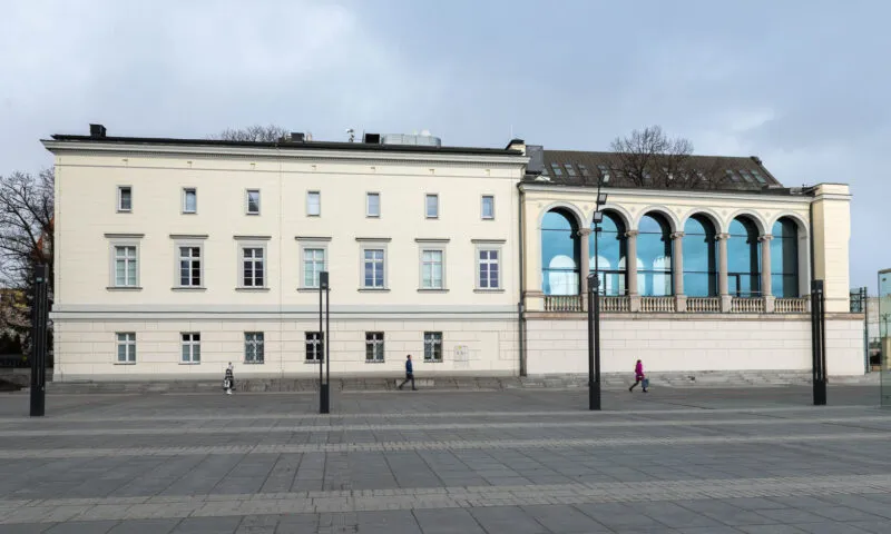 Zdjęcie przedstawia budynek Muzeum Teatru. Przed nim znajduje się deptak, a sam budynek jest w kształcie prostopadłościanu, z tego lewa jego część posiada liczne, ustawione symetrycznie obok siebie okna, a druga prawa część, składa się z sześciu dużych okien, które u górnej swojej części są zaokrąglone.