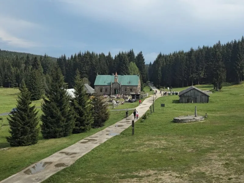 zdjęcie przedstawia drogę do schroniska otoczoną polami, na końcu drogi znajduję się schronisko z zielonym dachem
