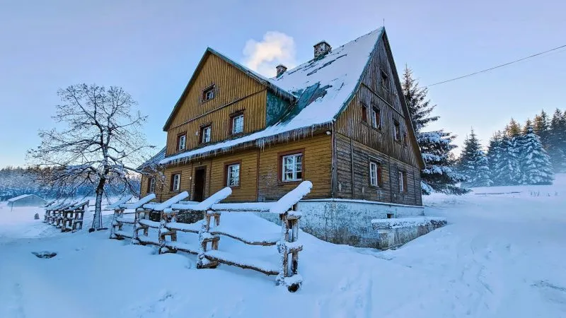 drewniane schronisko ukazane na zdjęciu od boku, pokryte śniegiem