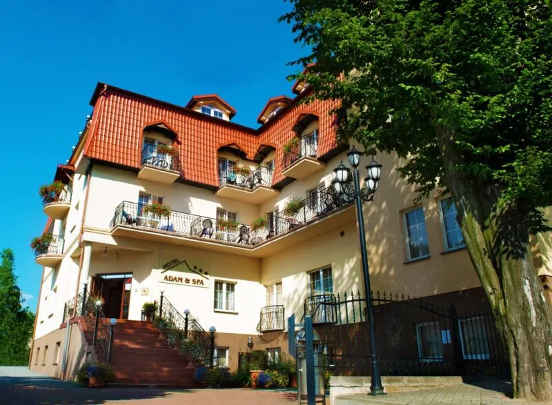 Wejście główne do hotelu z logo i nazwą hotelu. Budynek trójkondygnacyjny, na planie prostokąta.