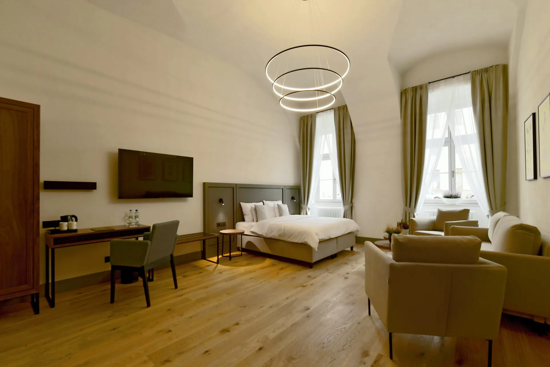 Duży, jasny, przestronny pokój hotelowy z łóżkiem podwójnym oraz częścią wypoczynkową.