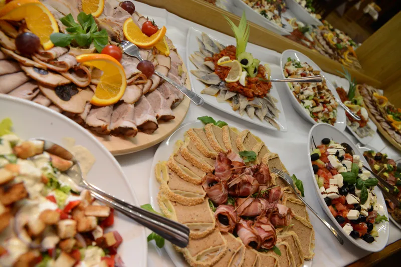 Stół zastawiony zimnymi przekąskami. Paleta wędlin, mini koreczki, śledzie, pasztety.