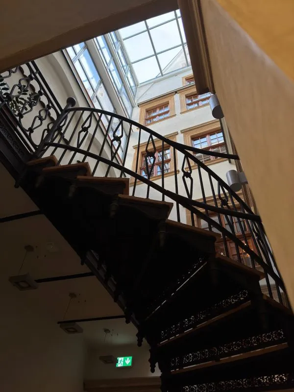 Obrazek przedstawia kręcone schody prowadzące na górne poziomy muzeum farmacji, wszystko jest oświetlone przez przeszklony dach.