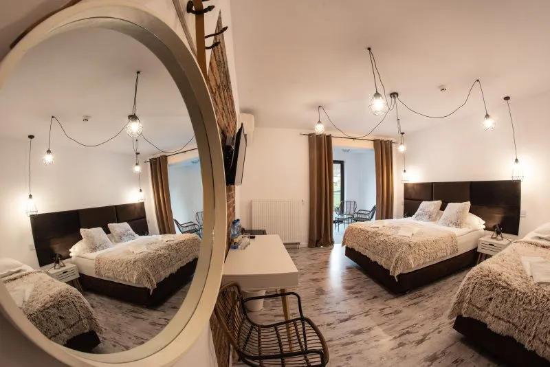 Pokój hotelowy z dwoma łóżkami, wiklinowym krzesłem oraz okrągłym lustrem.