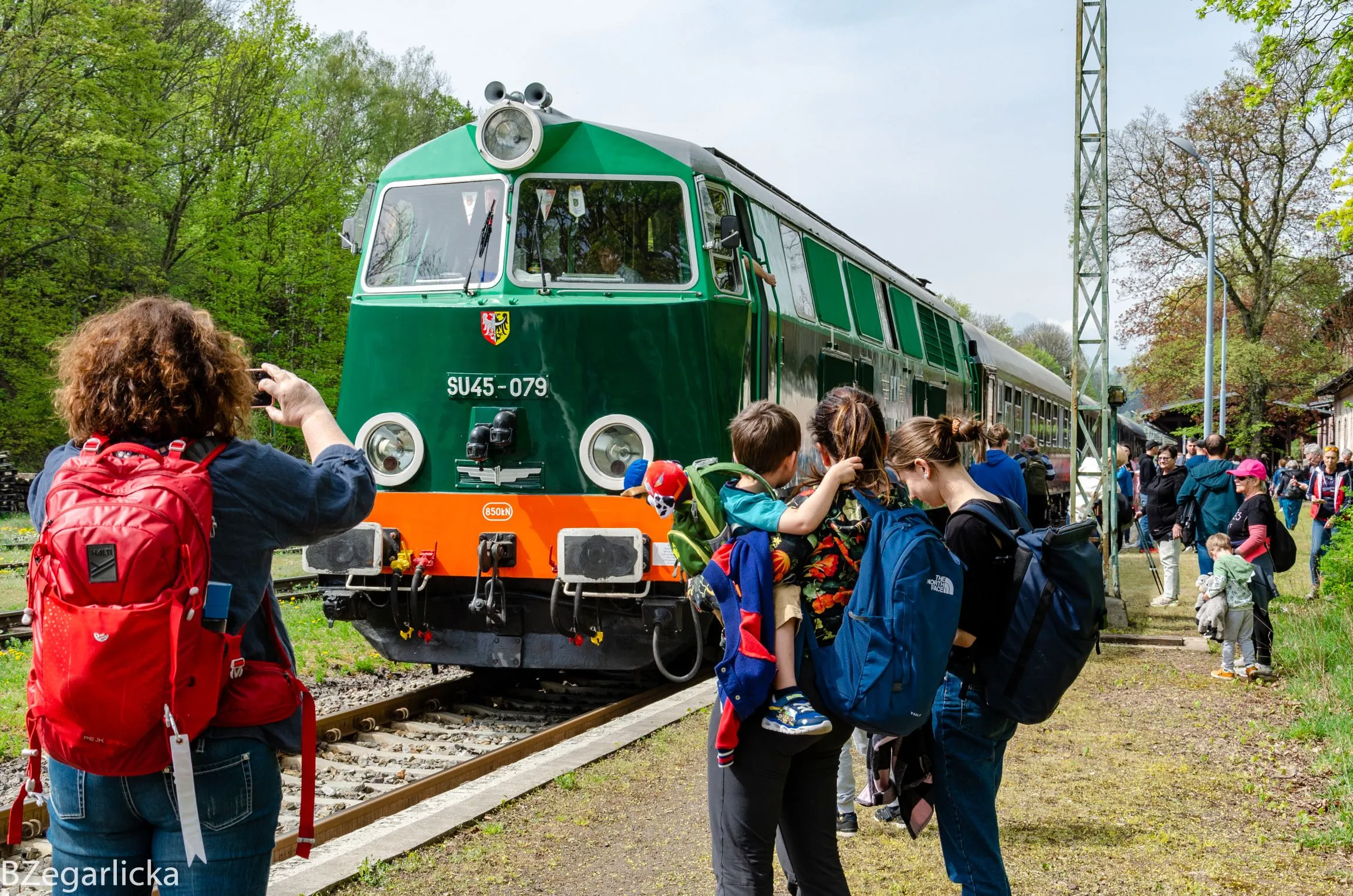 Zdjęcie przedstawia turystów stojących na peronie i fotografujących zabytkowy pociąg