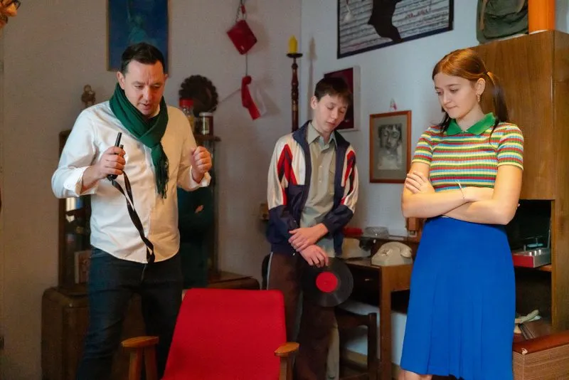 Un uomo con degli attrezzi parla con due giovani in un appartamento d'epoca, ricreando una scena per il film del Centro di Storia Zajezdnia.